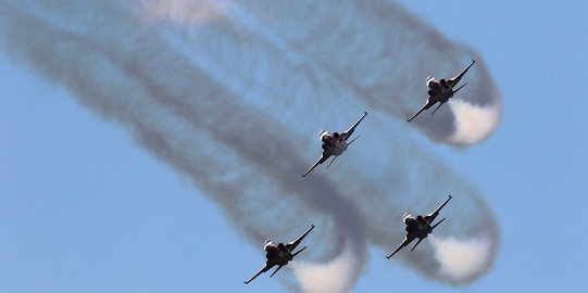Vier Militärflugzeuge fliegen Kunstflüge und hinterlassen sichtbare Emissionen