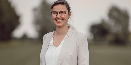 Kerrin Langer_Profilfoto Kerrin Langer vor unscharfem Hintergrund, wie sie in die Kamera lacht.