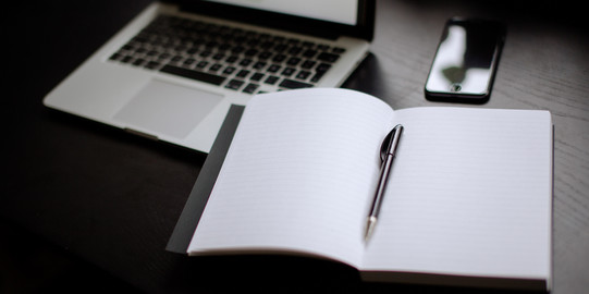 Turned on laptop, smartphone and notebook with pen lying on a table.